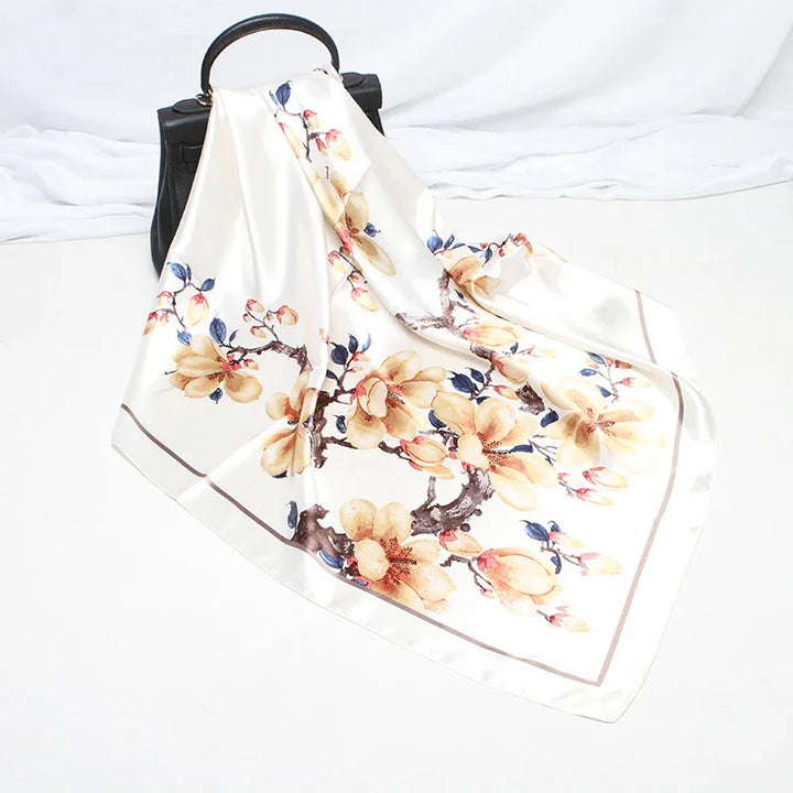 Silk scarf with beige floral print draped over black handbag on white background