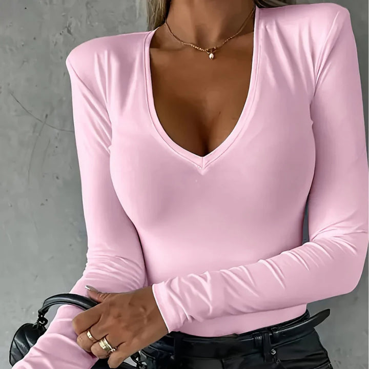 Woman wearing light pink long-sleeve V-neck top with gold necklace and black leather pants