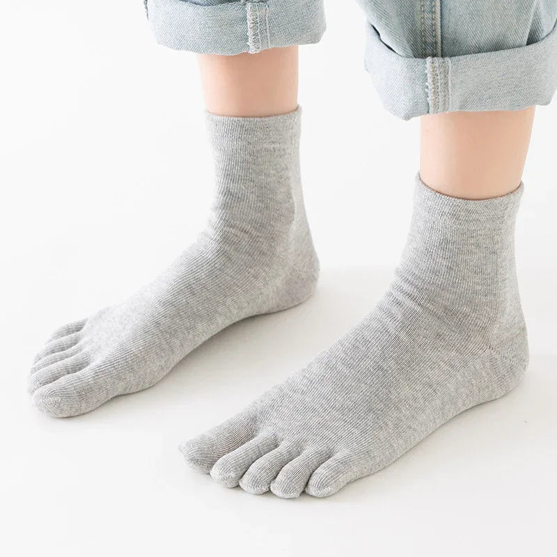 Feet wearing light gray toe socks with rolled-up light blue denim jeans on white background