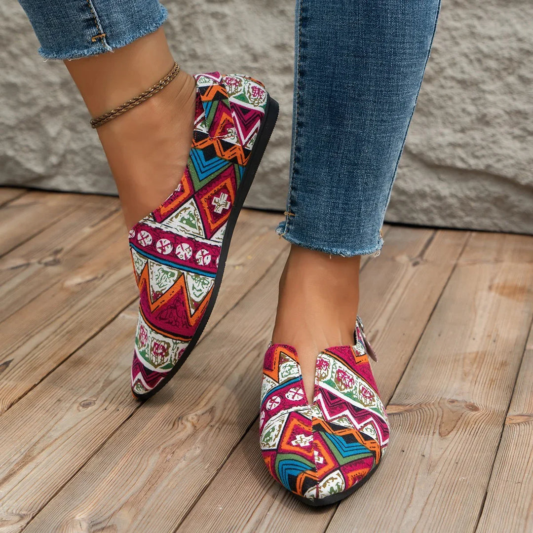 Close-up of colorful patterned slip-on shoes worn with blue jeans on wooden floor