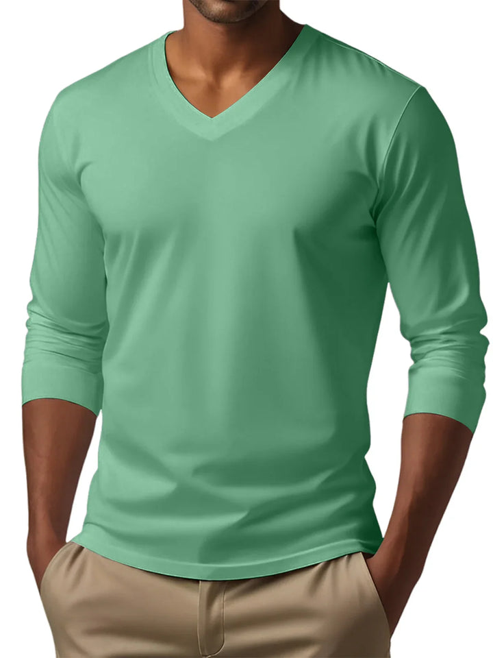 Man wearing a mint green V-neck long sleeve shirt with beige pants hands in pockets