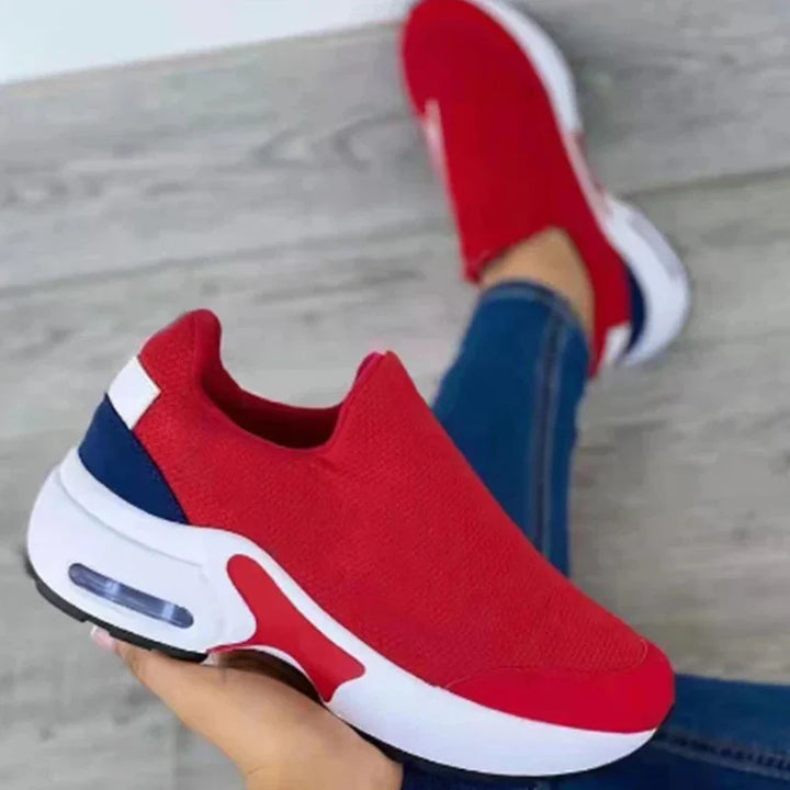 Red slip-on sports sneakers with white soles and navy heel accents worn with blue jeans