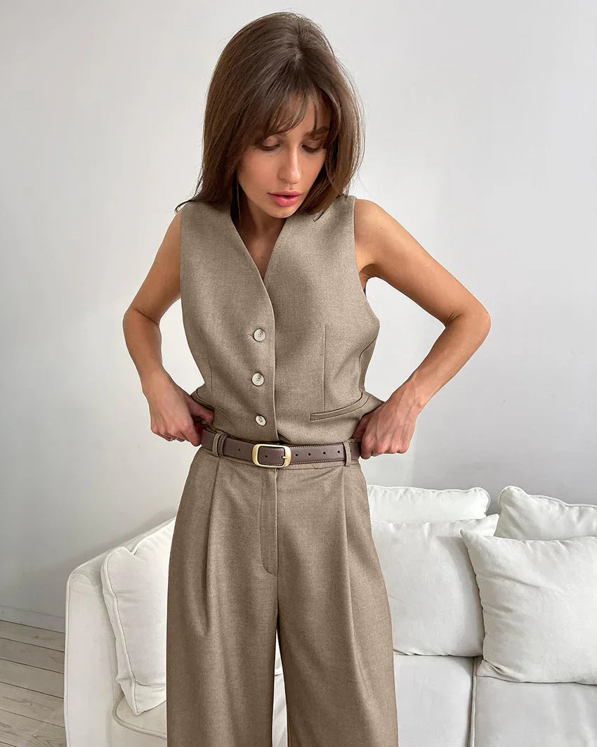 Woman wearing taupe sleeveless buttoned vest and wide-leg pants with brown belt in minimalist living room