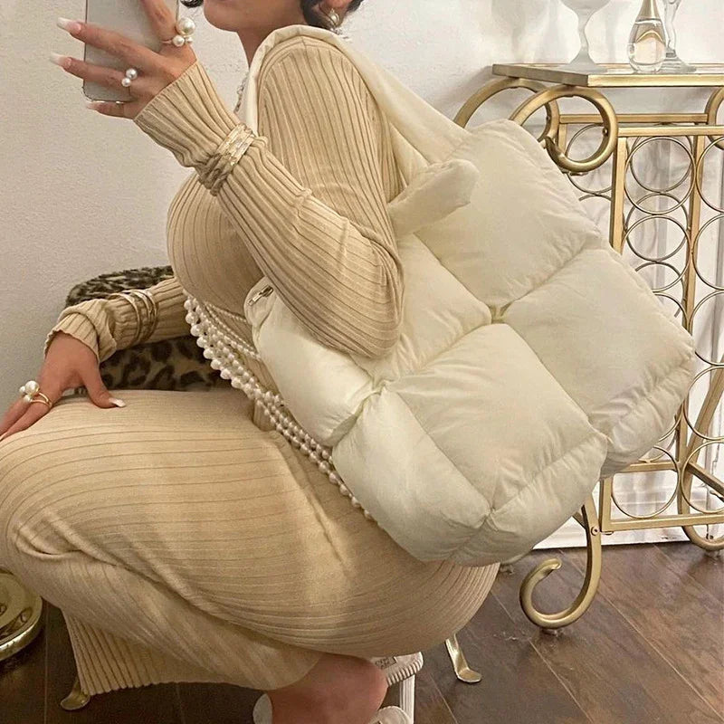 Woman wearing beige ribbed knit dress with pearl jewelry holding cream puffer shoulder bag indoors