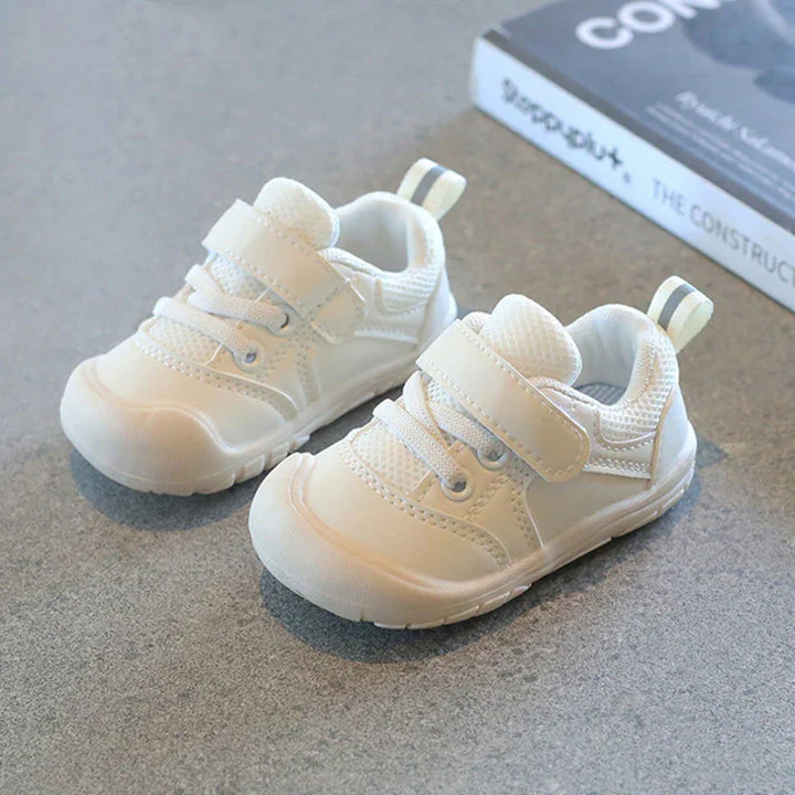 Pair of white toddler sneakers with Velcro straps and mesh details on grey surface