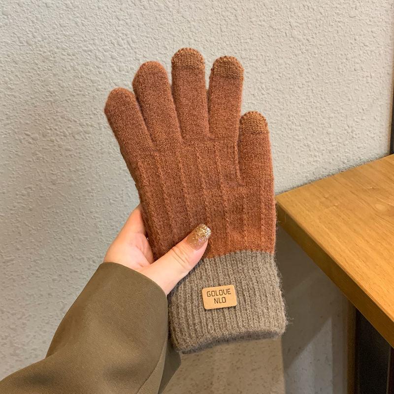 Hand holding warm brown knit gloves with gray cuffs and a small leather label indoors