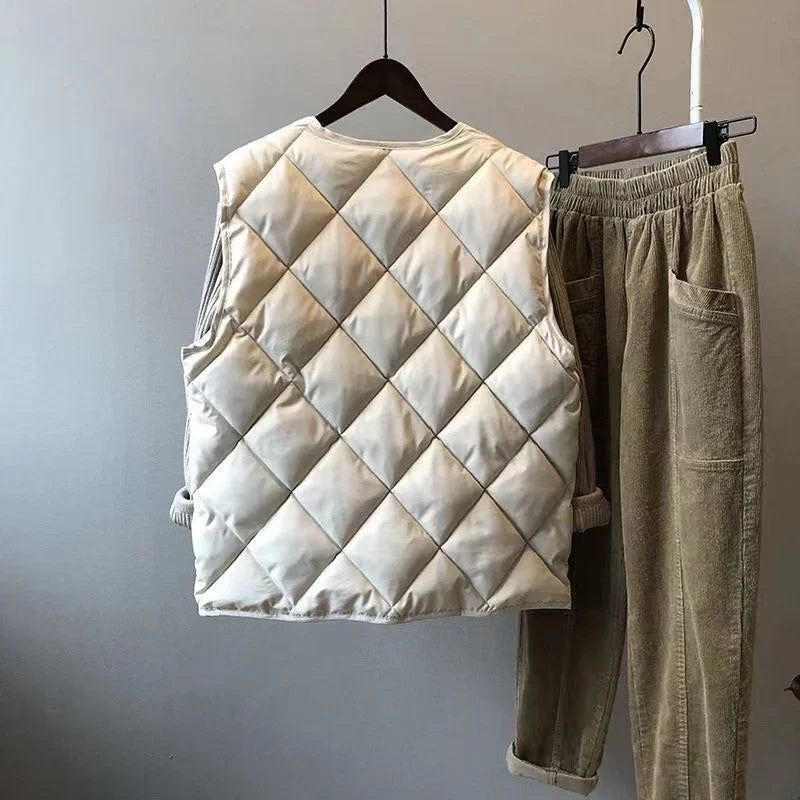 Beige quilted sleeveless vest and khaki corduroy pants hanging on black hangers against gray wall