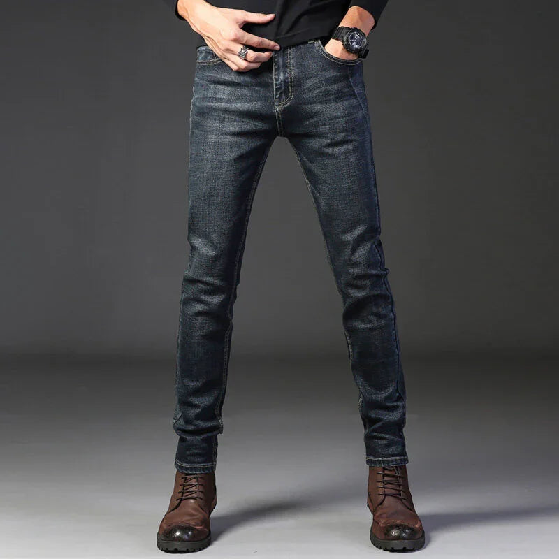 Close-up of man wearing dark slim-fit jeans and brown leather boots against gray background