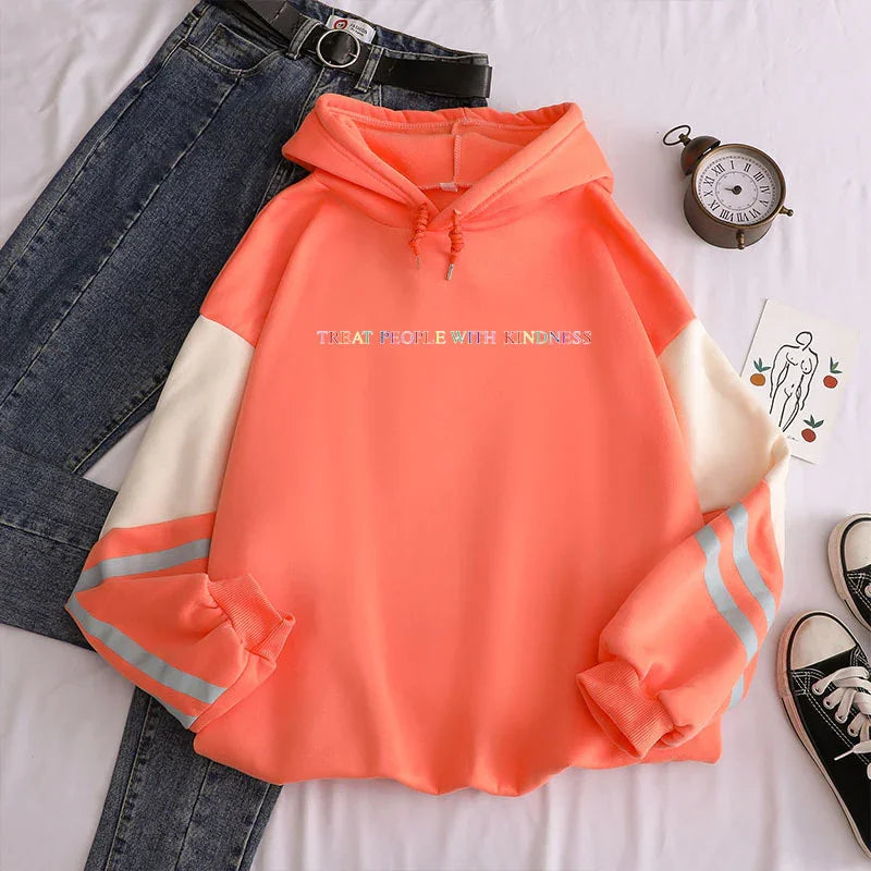 coral orange hoodie with white and grey striped sleeves saying 'Treat People With Kindness', paired with dark blue jeans and black sneakers