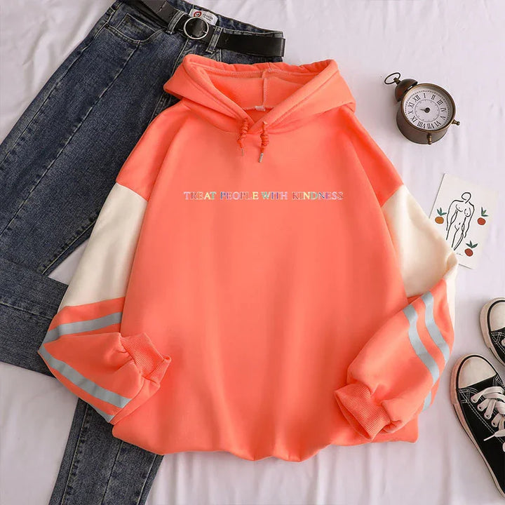 coral orange hoodie with white and grey striped sleeves saying 'Treat People With Kindness', paired with dark blue jeans and black sneakers