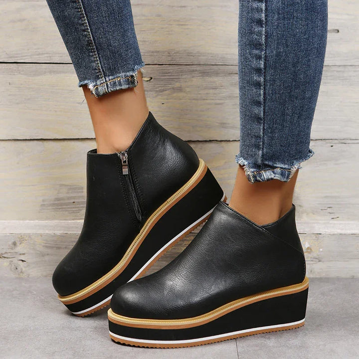 Black wedge ankle boots with side zipper worn with frayed hem blue skinny jeans on wooden floor