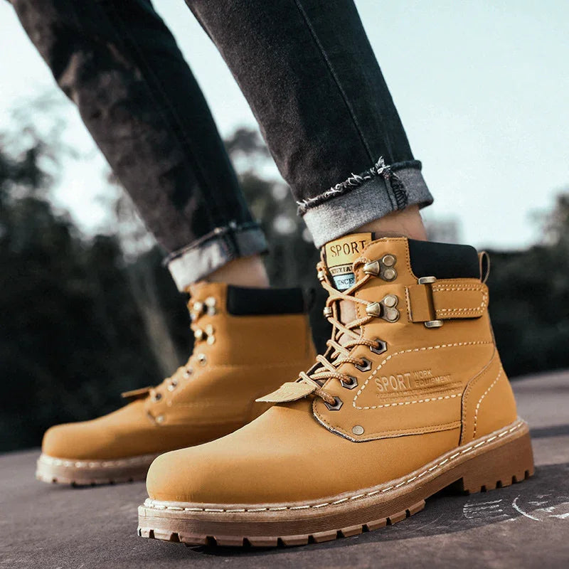 Close-up of tan sport work boots with black padded collars worn with rolled-up black jeans outdoors
