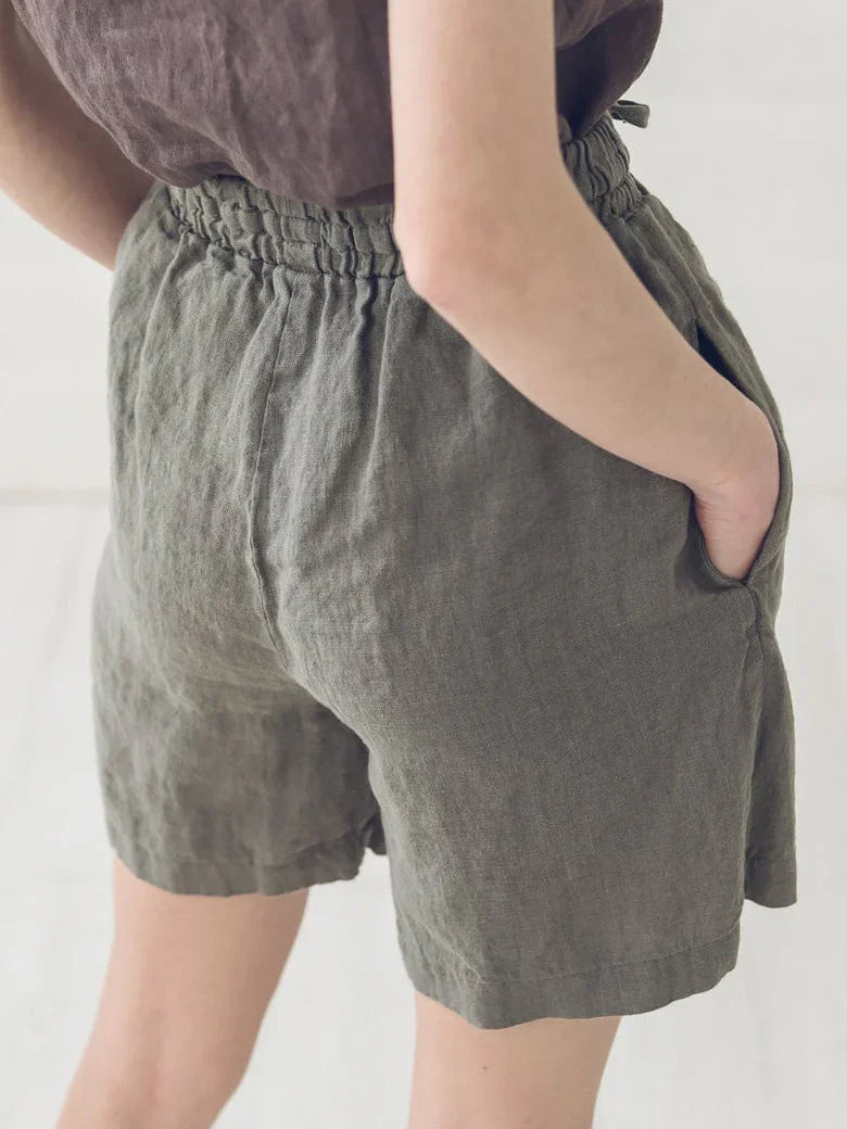 Close-up of person wearing olive green linen shorts with elastic waistband and side pockets