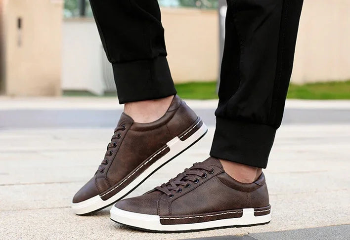 Brown leather casual sneakers with white sole worn with black pants outdoors on pavement