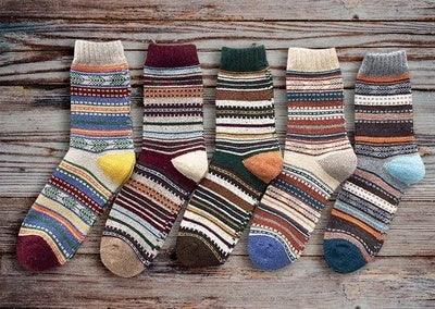 Five pairs of colorful striped wool socks laid out on a rustic wooden surface
