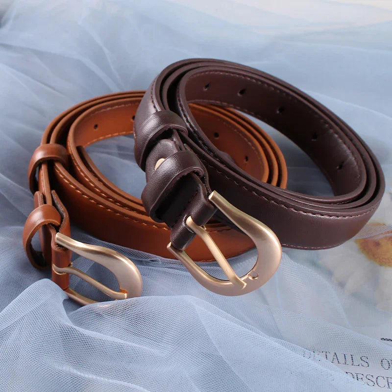 Two rolled leather belts in brown and dark brown with gold buckles on light blue fabric