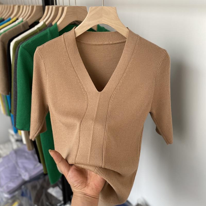 Hand holding beige ribbed short sleeve V-neck knit top on wooden hanger with colorful tops in background