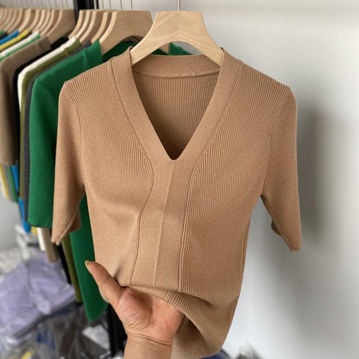 Hand holding beige ribbed short sleeve V-neck knit top on wooden hanger with colorful tops in background