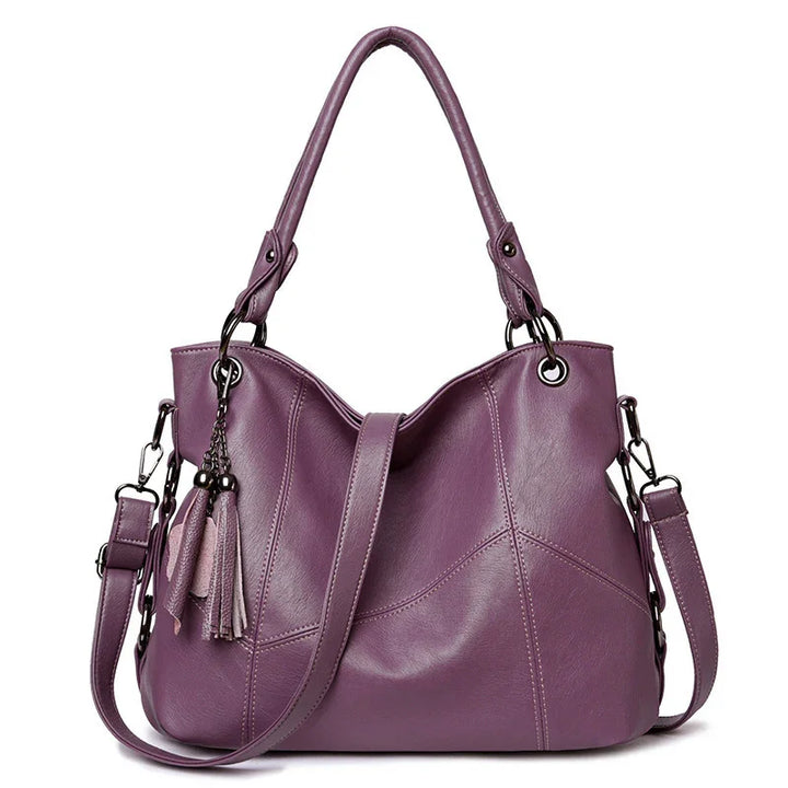 Purple leather handbag with top handles, detachable shoulder strap, and decorative tassels