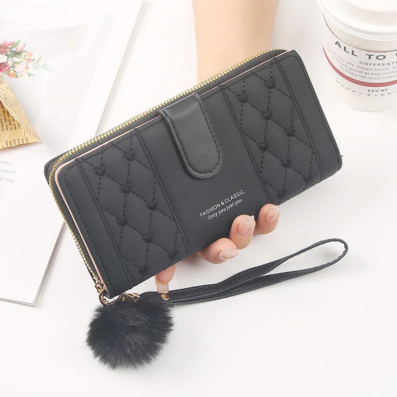 Black quilted leather wallet with wrist strap and fluffy pom pom keychain, held in hand
