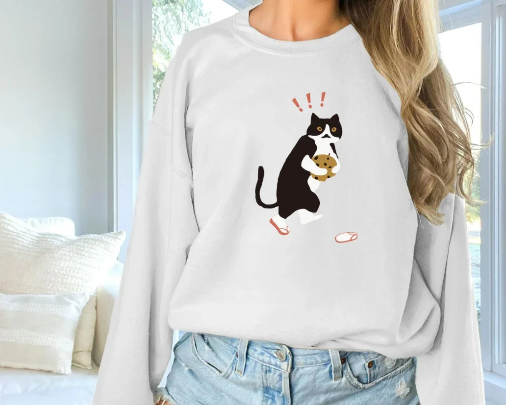 Woman wearing white sweatshirt with funny black and white cat holding a cookie graphic indoors