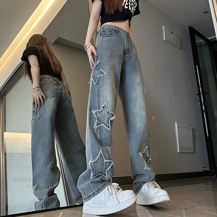Low-angle view of woman wearing star-patched wide-leg jeans and white sneakers in modern room