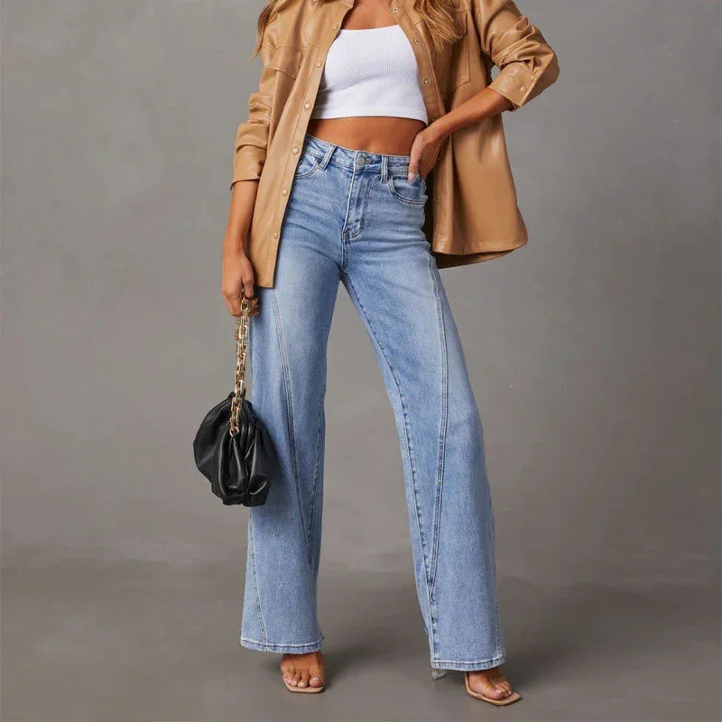 Woman wearing light blue wide-leg jeans, white crop top, tan leather jacket, holding black purse with gold chain
