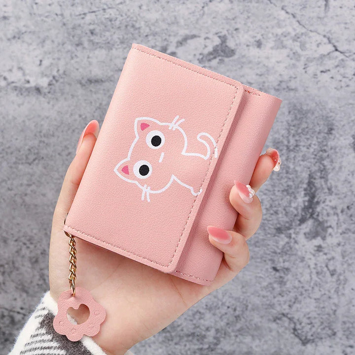 Hand holding a pink wallet with cartoon cat design and flower keychain against gray marble background