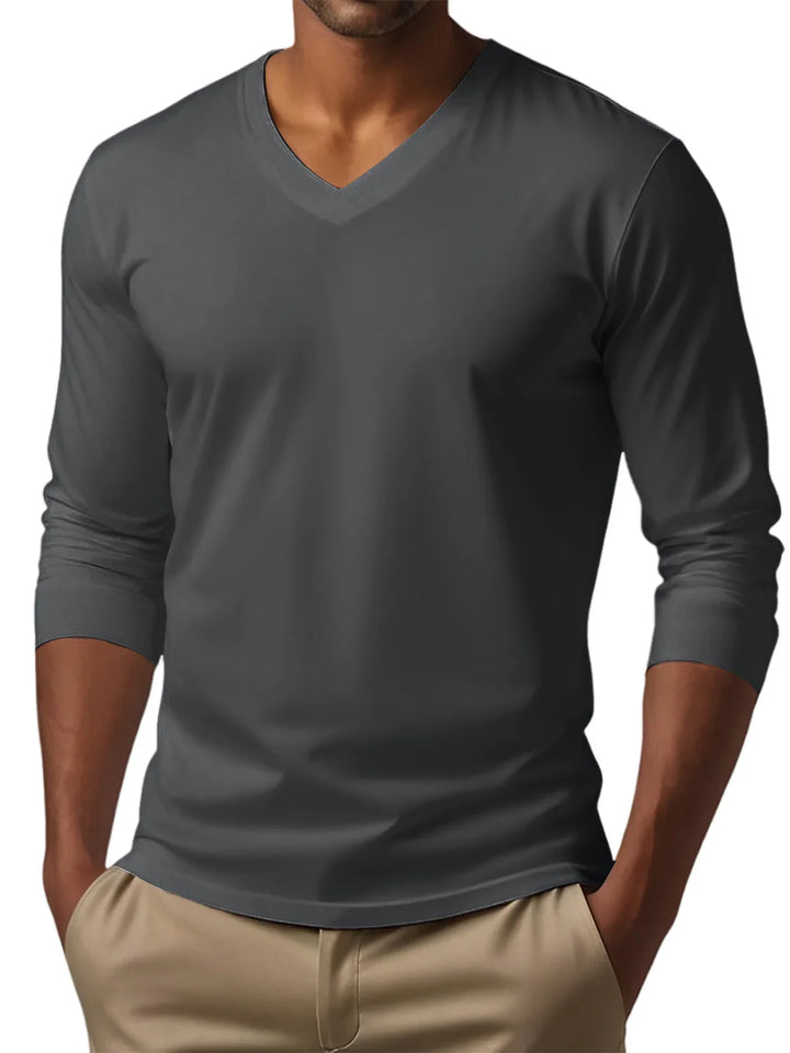 Man wearing a dark gray V-neck long sleeve t-shirt tucked into beige pants with hands in pockets