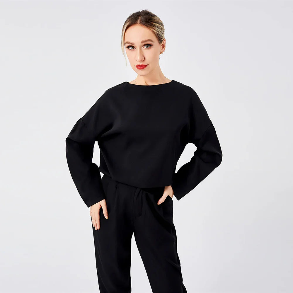 Woman wearing black long sleeve top and pants posing against plain white background