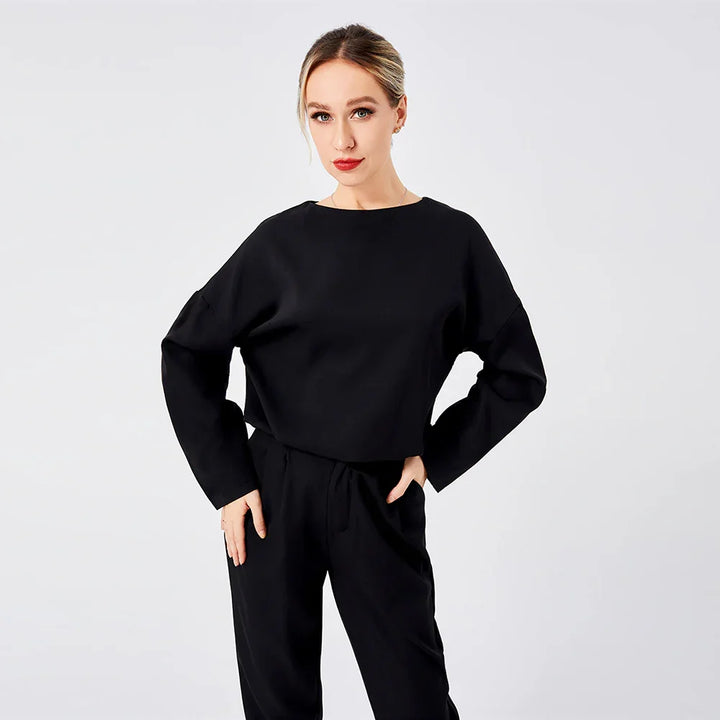 Woman wearing black long sleeve top and pants posing against plain white background
