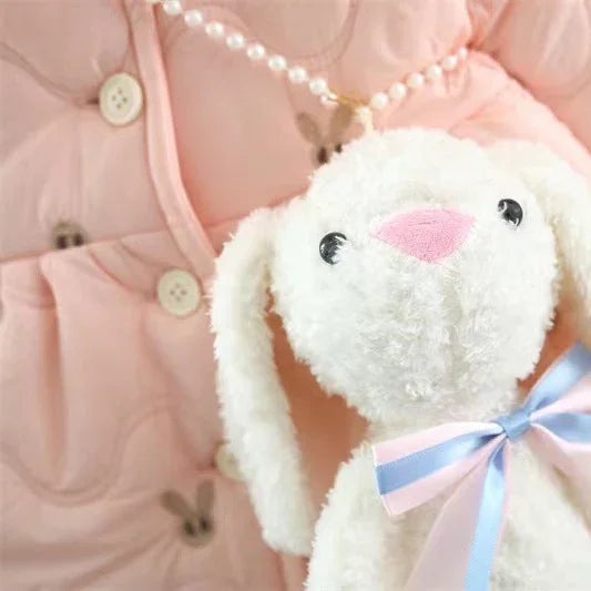 White fluffy bunny plush toy with pink nose and blue-pink ribbon, on pink quilted fabric background