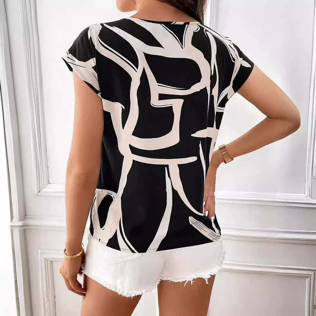 Woman wearing black and white abstract print top and white frayed denim shorts in bright room