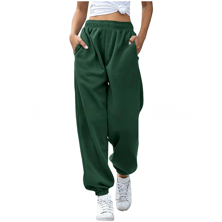 Woman wearing dark green loose sweatpants with elastic waistband and cuffs, paired with white sneakers
