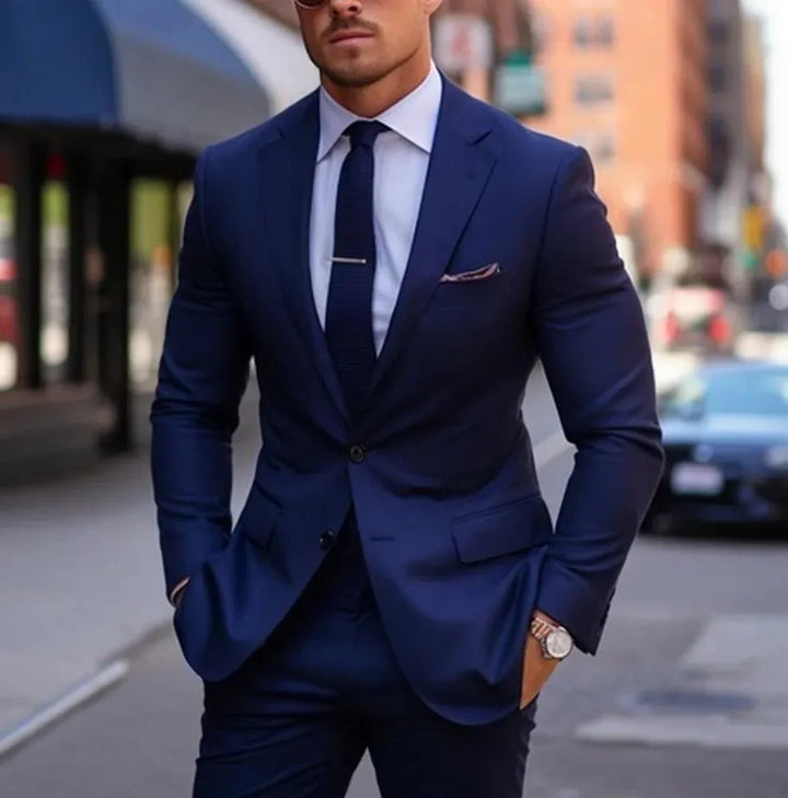 Man wearing a tailored navy blue suit with matching tie, white dress shirt, and watch on city street