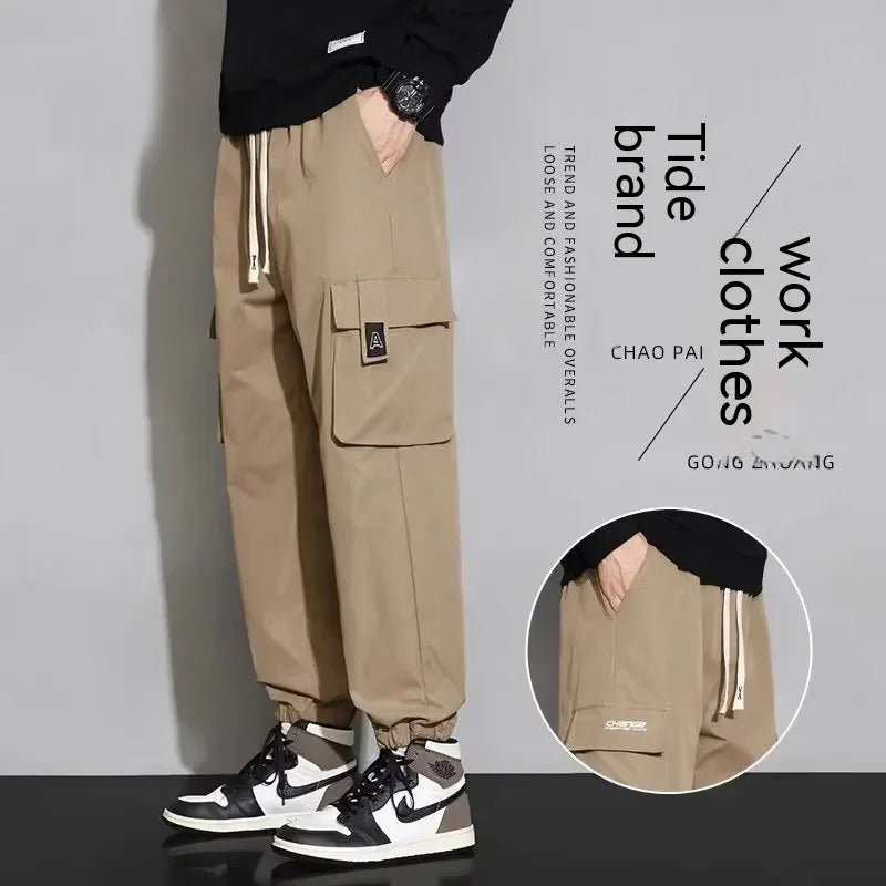 Men's beige work cargo pants with large pockets and elastic cuffs, styled with black and white sneakers