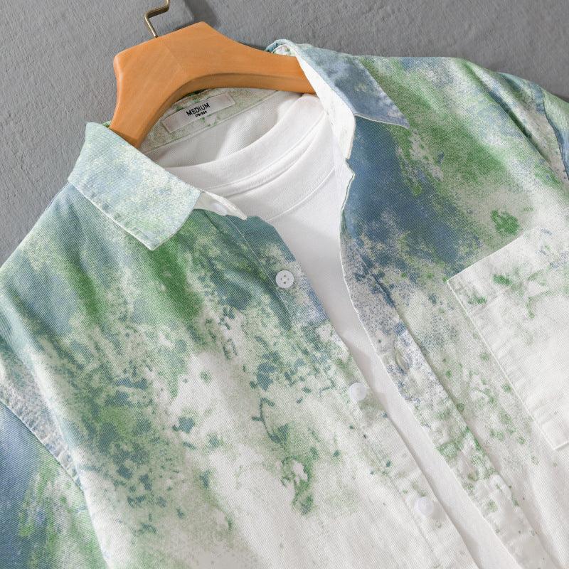 Close-up of green and blue tie-dye button-up shirt layered over white T-shirt on wooden hanger