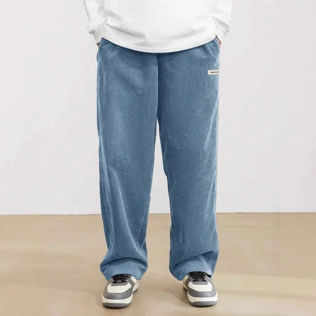 Person wearing loose blue corduroy pants with hands in pockets and white sneakers