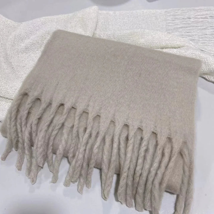 Folded beige wool scarf with fringed ends on a white textured fabric background