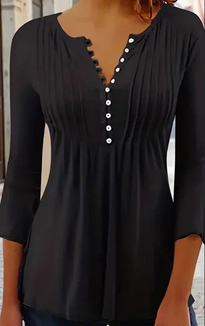 Woman wearing a black long-sleeve blouse with white buttons and pleated details
