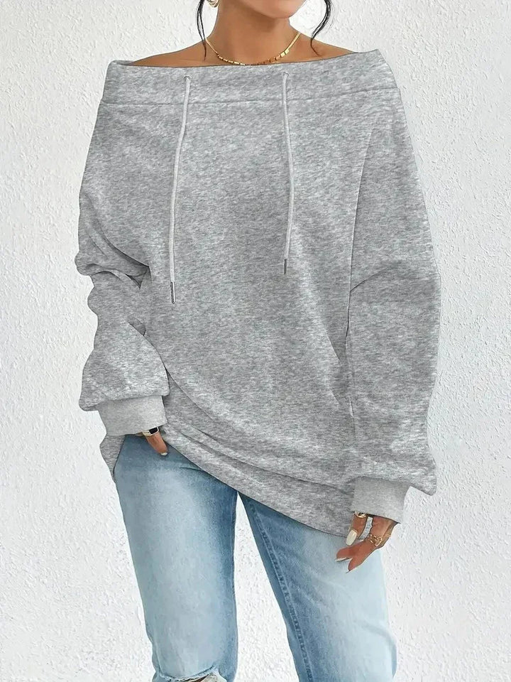 Woman wearing light gray off-shoulder sweatshirt with drawstrings and light blue ripped jeans