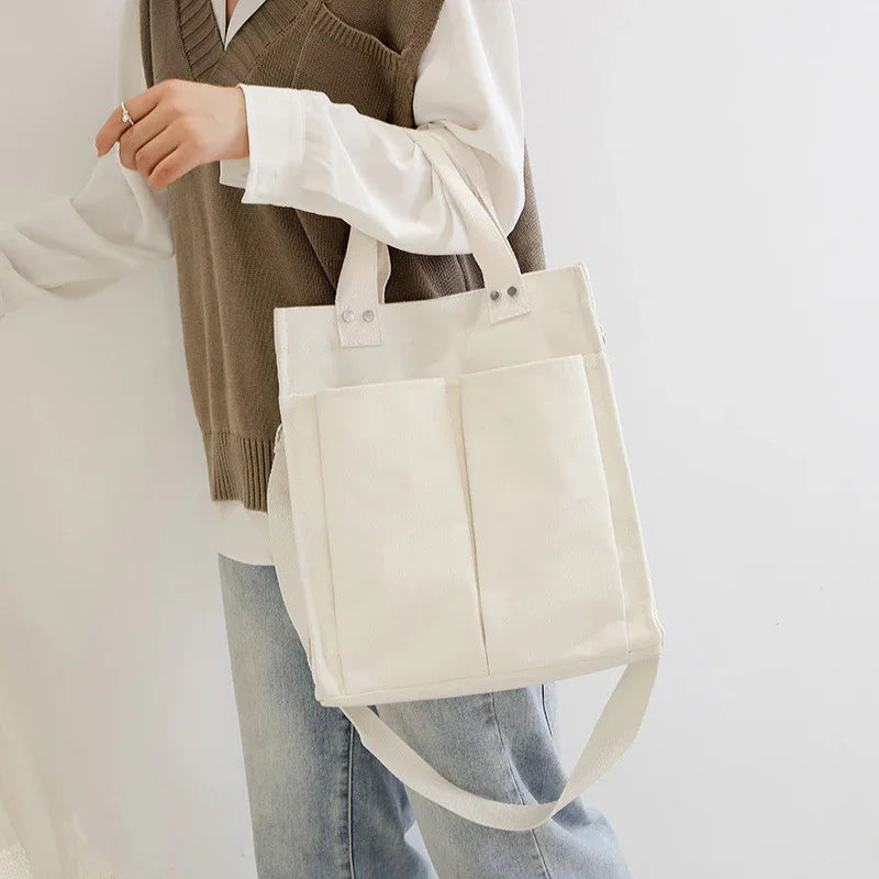 Person wearing brown vest and white shirt holding a cream canvas tote bag with front pockets