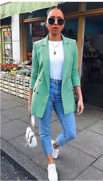 woman wearing mint green blazer, white t-shirt, blue jeans, white sneakers, and round sunglasses walking outside market