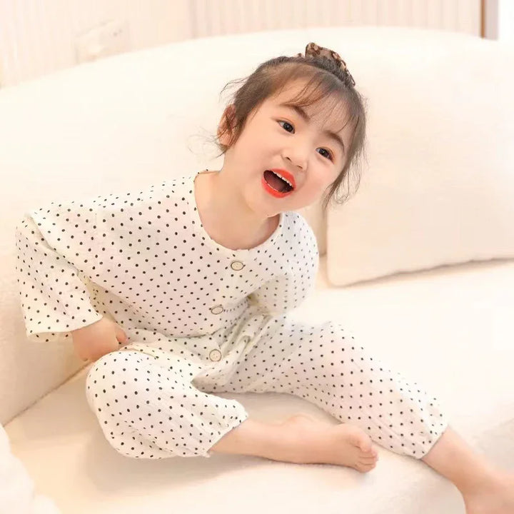 Happy toddler girl wearing white polka dot pajamas sitting on a light couch indoors