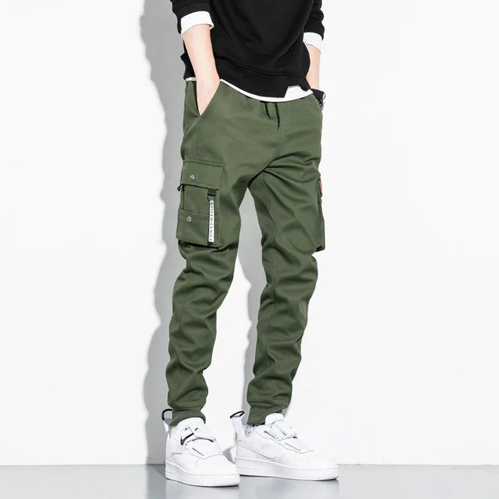 man wearing green cargo pants with flap pockets and white sneakers on white background