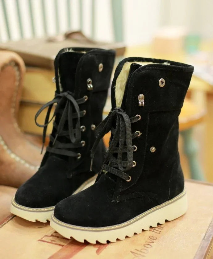 Black suede winter boots with faux fur lining and white rugged soles on wooden surface
