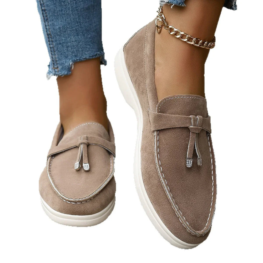 Beige suede moccasin shoes with white stitching and tassels, worn with frayed hem blue jeans and gold chain anklet