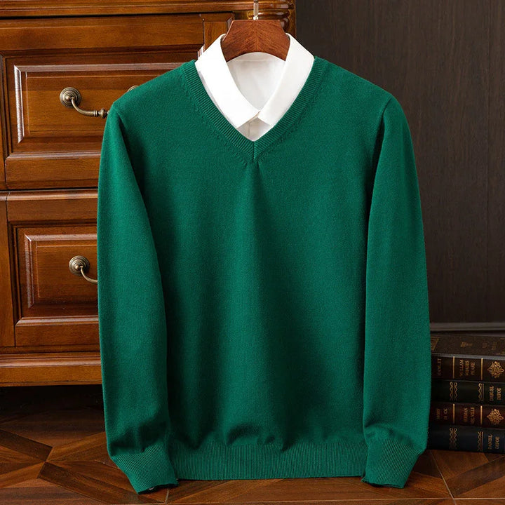 Green V-neck sweater layered over white collared shirt, displayed on wooden hanger with wooden drawer and books background