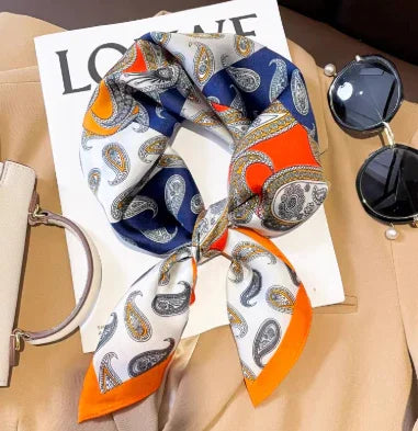 Colorful paisley silk scarf with orange, blue, and white sections on magazine and tan leather surface