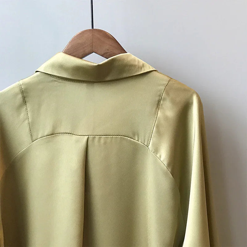 Back view of light green satin shirt on wooden hanger against plain wall